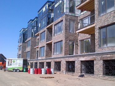 Stone-clad building under construction with barrels and equipment outside.