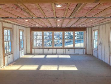 A room under construction with insulation and large windows letting in sunlight.