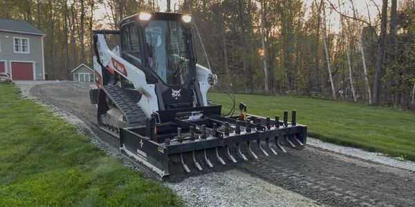 Compact track loader with a soil conditioner attachment working on a gravel path.