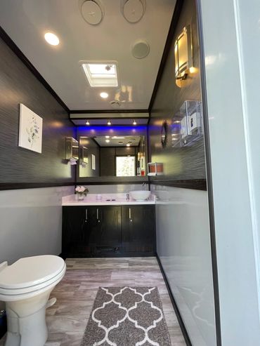 Interior of 2 stall restroom trailer. Two-toned gray with toilet, vanity sink area, and blue light.