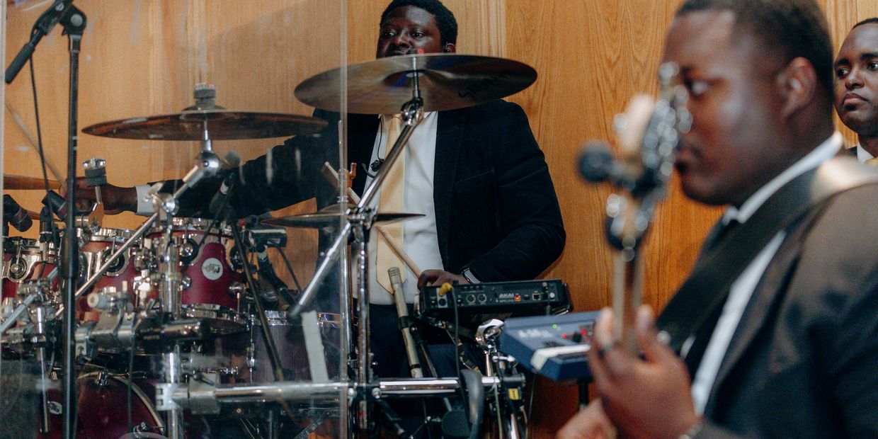 Musicians performing together with drums and guitar in a wooden-paneled room.
