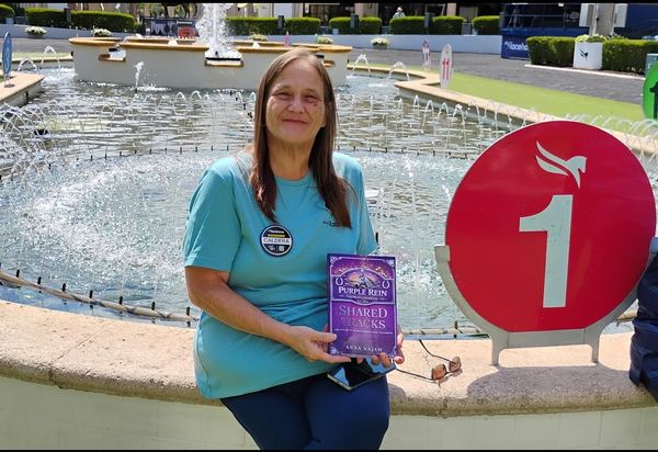 Woman holding a book by a fountain, smiling.