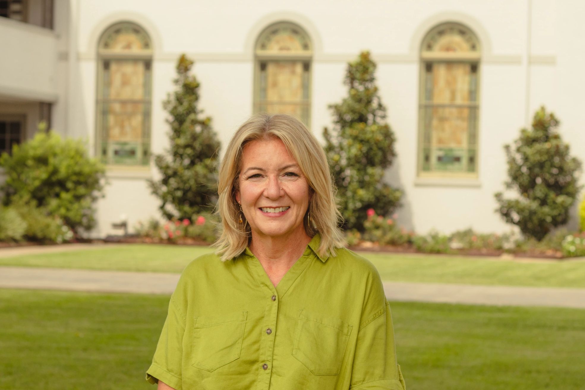 A woman smiling outdoors in a green shirt.