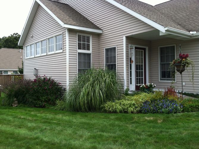 taupe-colored condominium with mature plants and lush green lawn