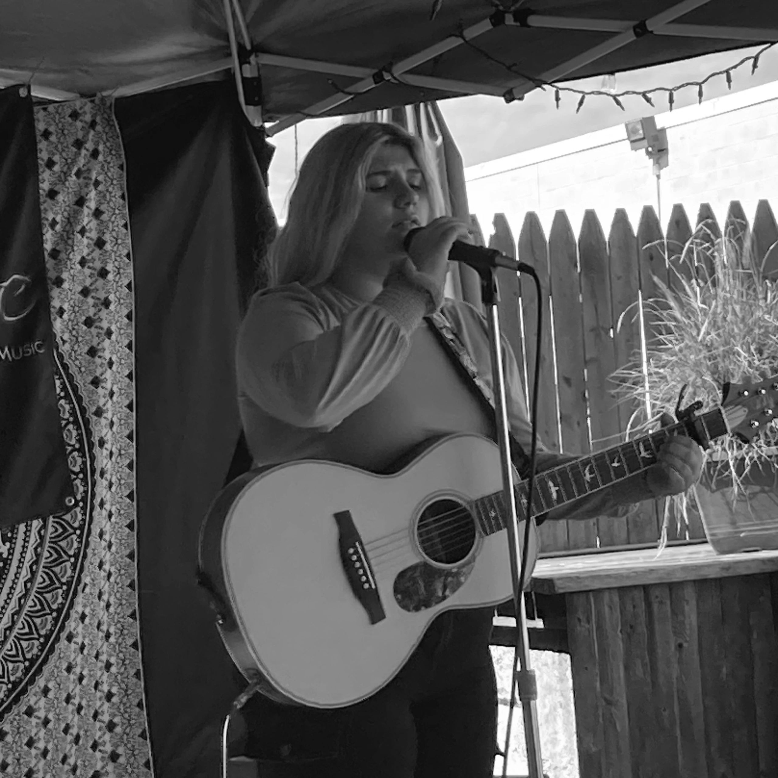 Black and white image of teen girl with blonde hair holding guitar in front of microphone stand