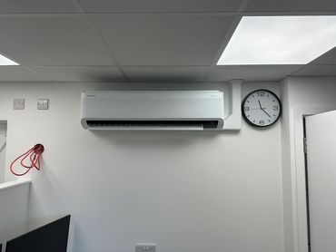 Wall-mounted air conditioner and clock in a plain room.