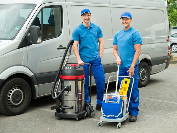 Two Happy Male Cleaners Standing With Cleaning Equipment In Front Of Van