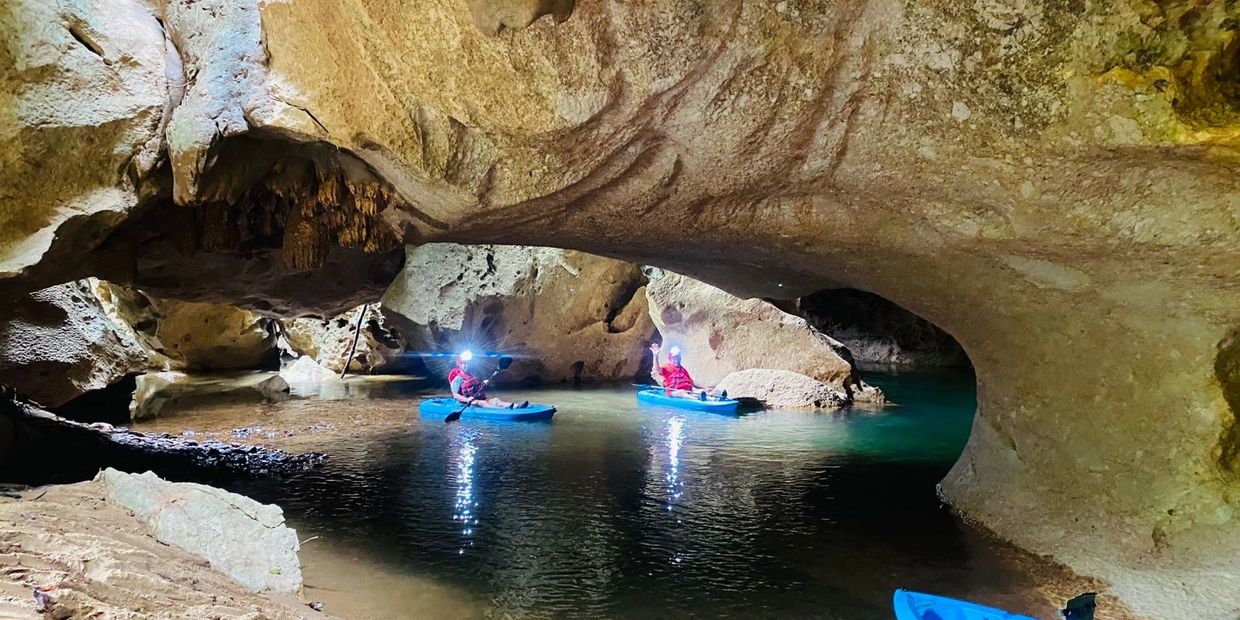 Two people kayaking inside a dimly lit cave with headlamps on.