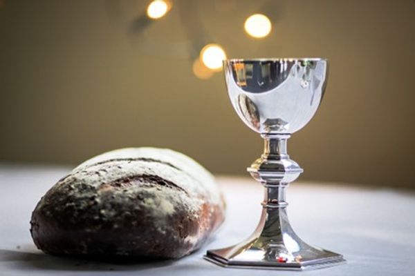 A loaf of bread and a silver chalice on a white cloth with blurred lights.
