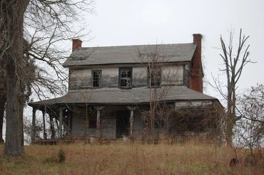 An old, abandoned two-story house with broken windows and overgrown vegetation.