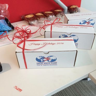 Three white gift boxes with red ribbons saying 'Happy Holidays 2016' on a desk.