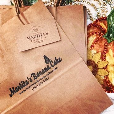 Brown paper bags from Martita's Banana Cake with logo and contact info.