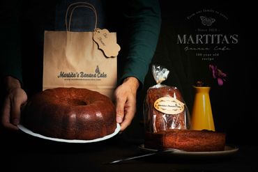 Martita's Banana Cake displayed with packaging and a yellow vase with flowers.