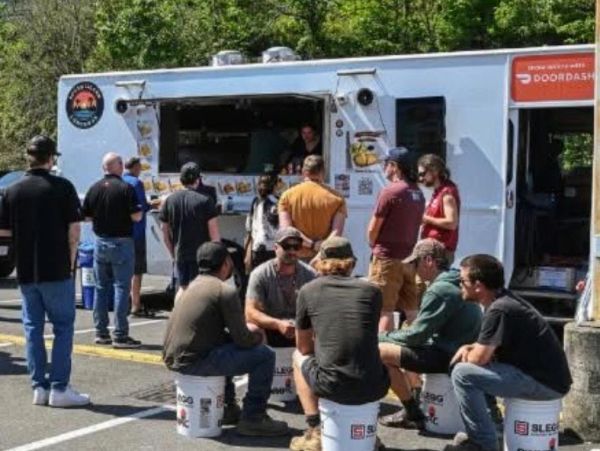 People gather around a food truck, some sitting on buckets, others standing in line.