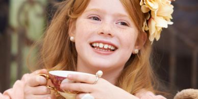 A joyful girl with red hair enjoying tea from a delicate cup.