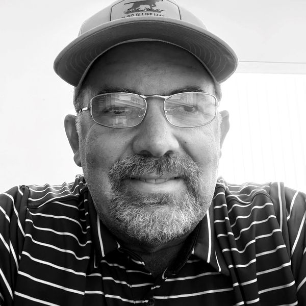 Smiling man wearing glasses and a striped polo shirt with a cap.