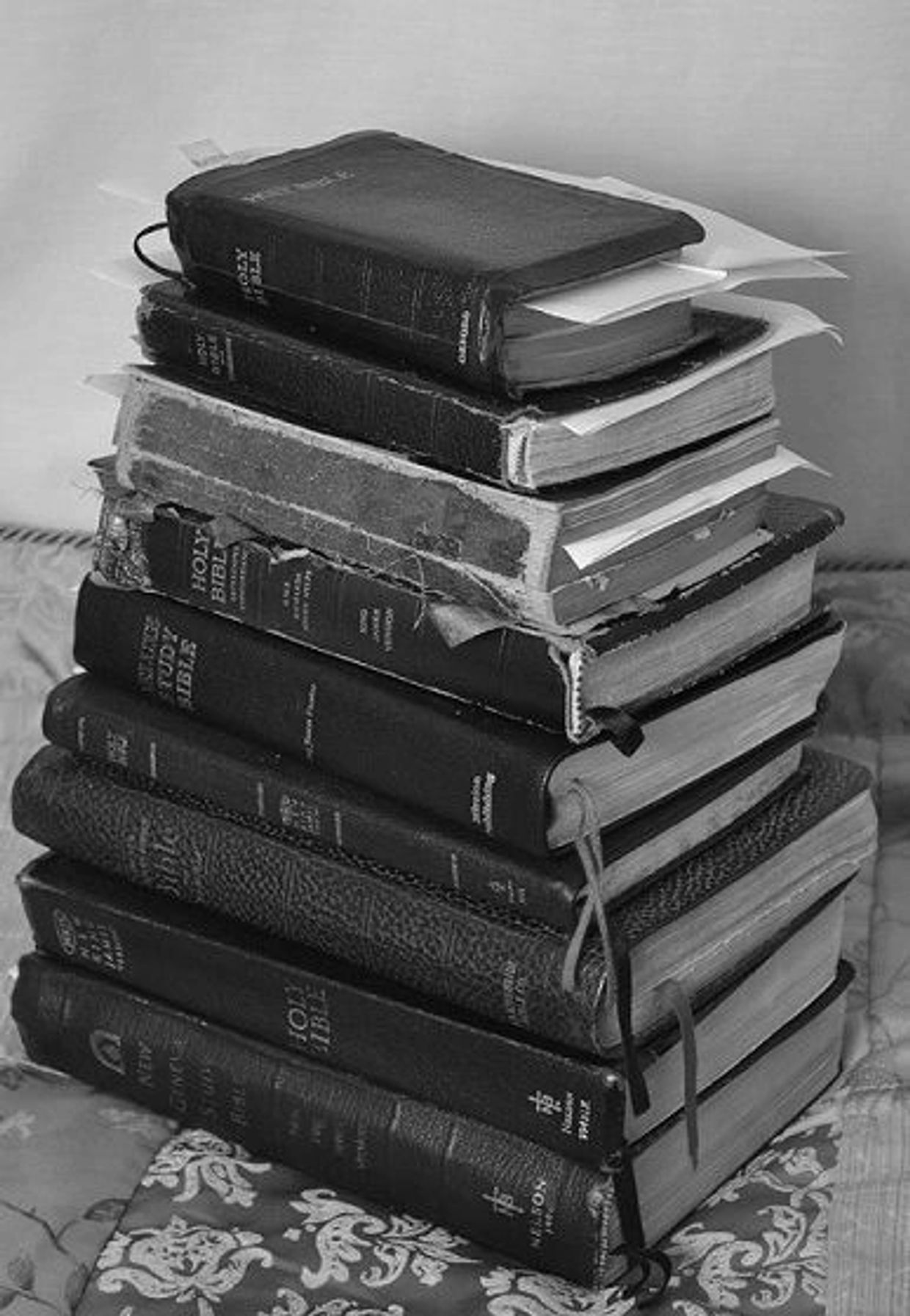 A stack of well-used Holy Bible books with bookmarks and inserted papers.