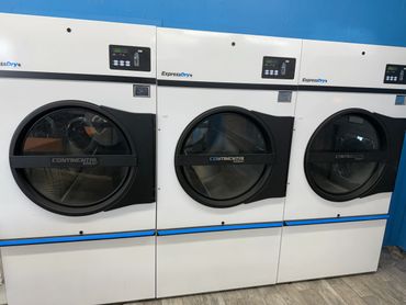 Three commercial dryers in a laundromat with blue walls.