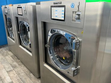 Row of industrial stainless steel washing machines in a laundromat.