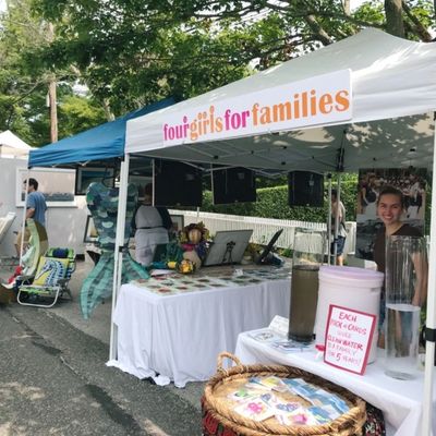 Outdoor booth with banner "four girls for families" at a fair or market.