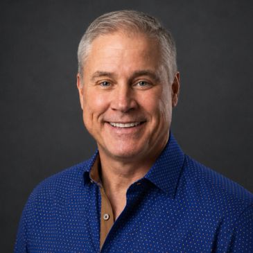 Smiling middle-aged man with gray hair wearing a blue shirt.