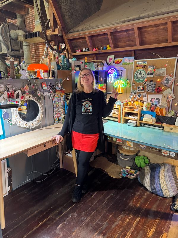 Woman smiling in a colorful, cozy workspace filled with decorations and neon signs.