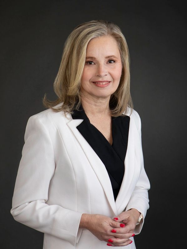 Professional woman in white blazer with black blouse against dark background.