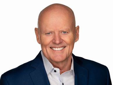 Smiling bald man in a navy blazer and white shirt against a white background.