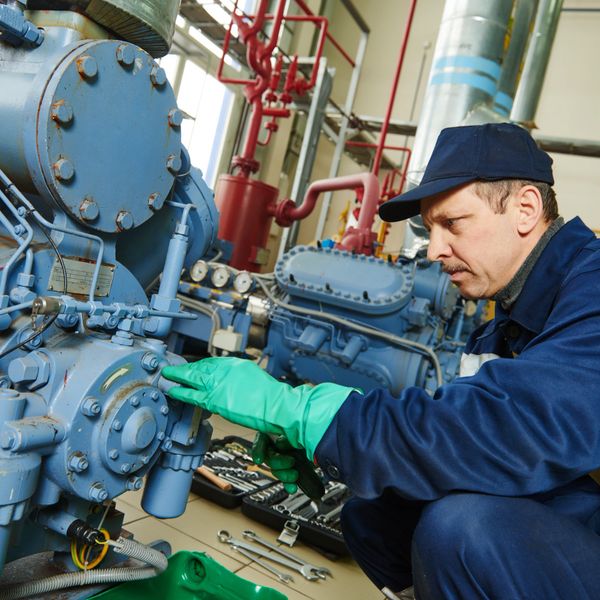 Technician repairing industrial machinery with tools and gloves.