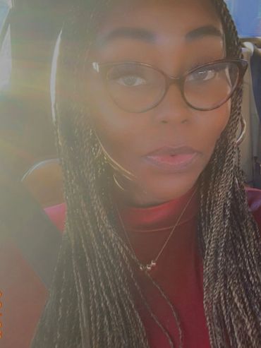 Woman with braided hair and glasses sitting in a car with sunlight flare.