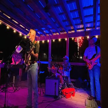 Country band performs under blue lights with fireworks in the background.