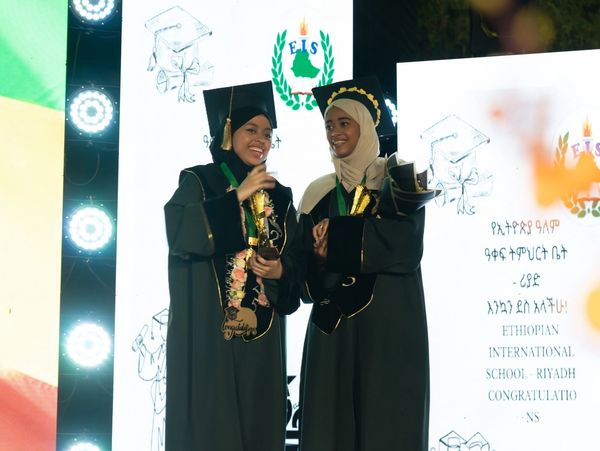 Two graduates in traditional attire celebrating with trophies and smiles.