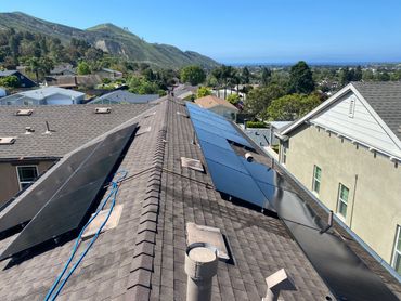 Solar panels installed on a residential rooftop with a scenic hillside background.