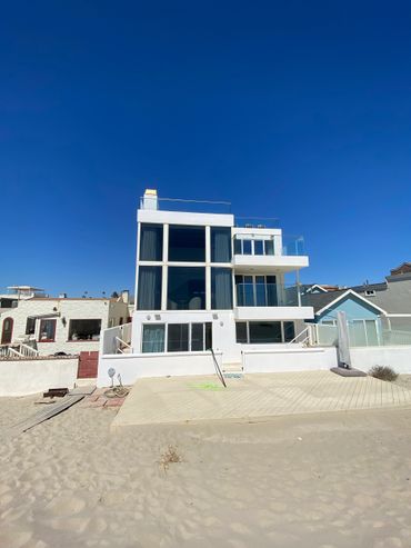 Modern white beachfront house with large glass windows under a clear blue sky.