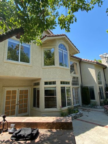 Sunlit backyard of a beige stucco house with large windows and a tiled patio.