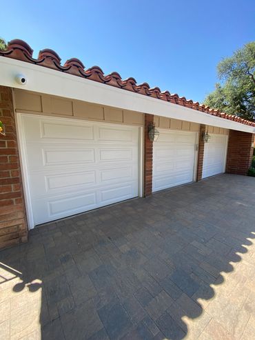 Three white garage doors with brick pillars and tiled roof under clear blue sky.