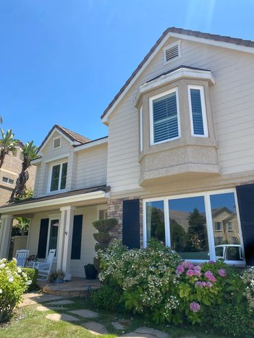 Two-story house with a porch, garden, and clear blue sky.