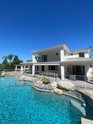 Modern two-story house with a clear blue pool under a bright sky.