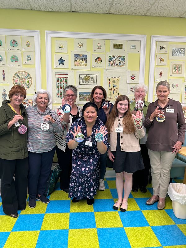 Group of people smiling with finished needlepoint ornaments
