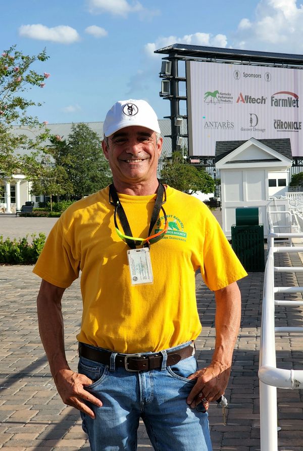 Smiling man in yellow shirt and white cap standing outdoors on a sunny day.
