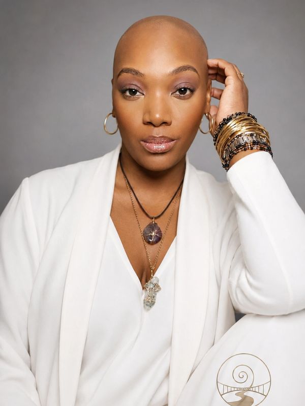 Confident woman with shaved head in white outfit with jewelry.