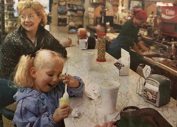 Image: happy little girl enjoys ice cream cone with grandmother while sitting at soda fountain