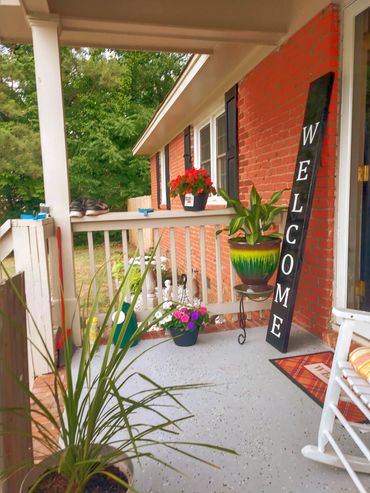 Cozy front porch with plants and a vertical welcome sign.