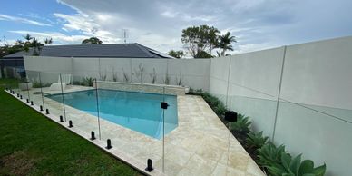 Modern backyard swimming pool with glass safety fence and tiled deck.