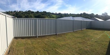 Newly laid sod in a backyard enclosed by a tall metal fence under a blue sky.