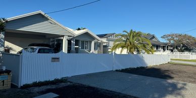 Modern suburban houses with white fences and a clear blue sky.