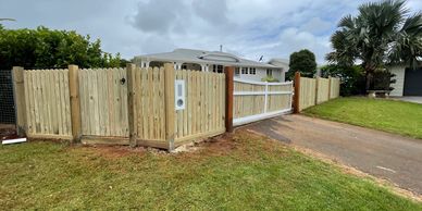 New wooden fence and gate enclosing a suburban house driveway and yard.
