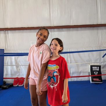 Two girls smiling inside a boxing ring.