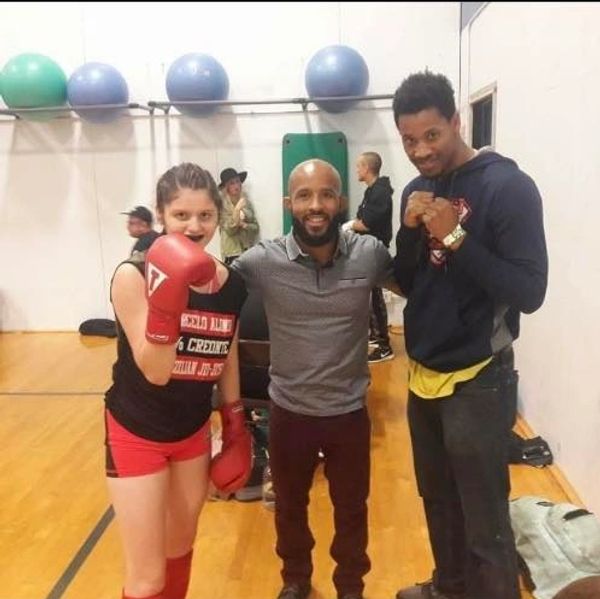 Three people posing in a gym, one wearing boxing gloves.