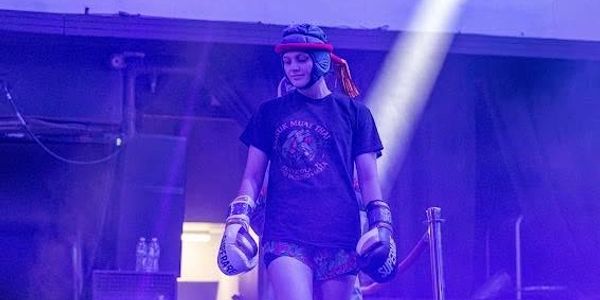 Female Muay Thai fighter walking with gloves and headgear.